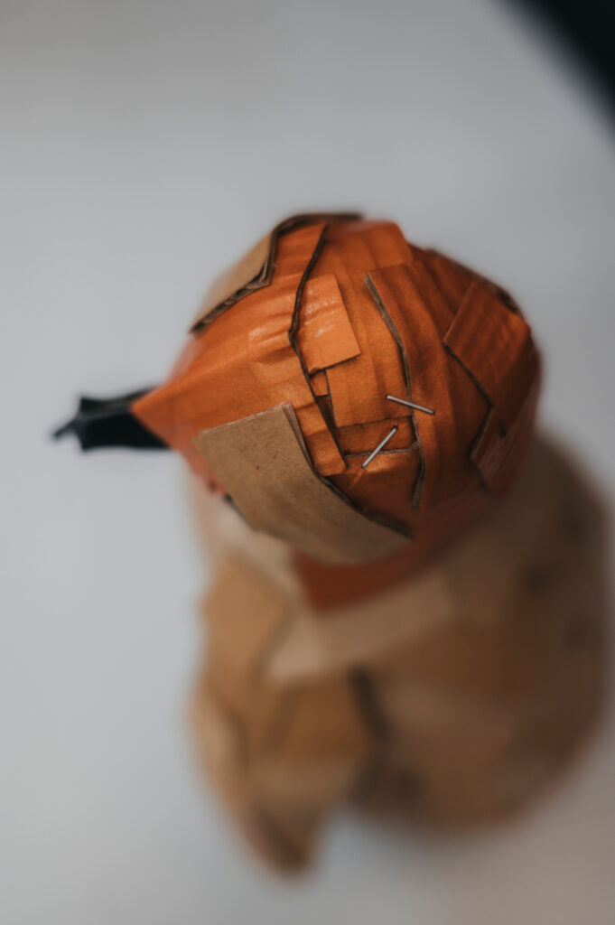 Detalle cabeza pingüino naranja tornasol. Escultura de cartón. Orgaz.