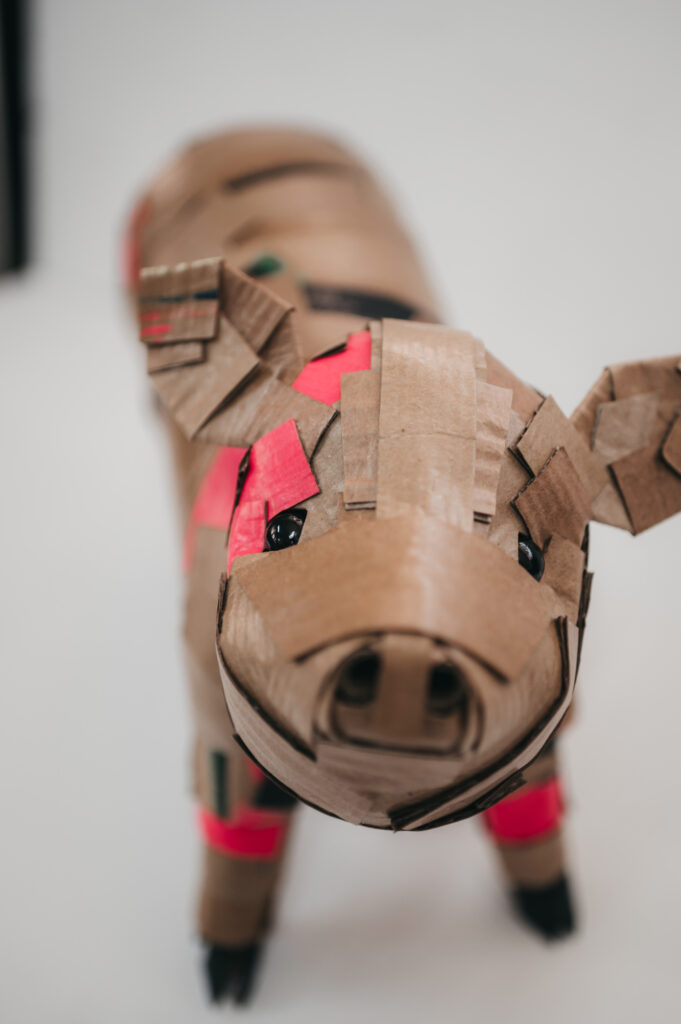 Cerdito en rosa entero, vista frontal. Escultura de cartón. Orgaz