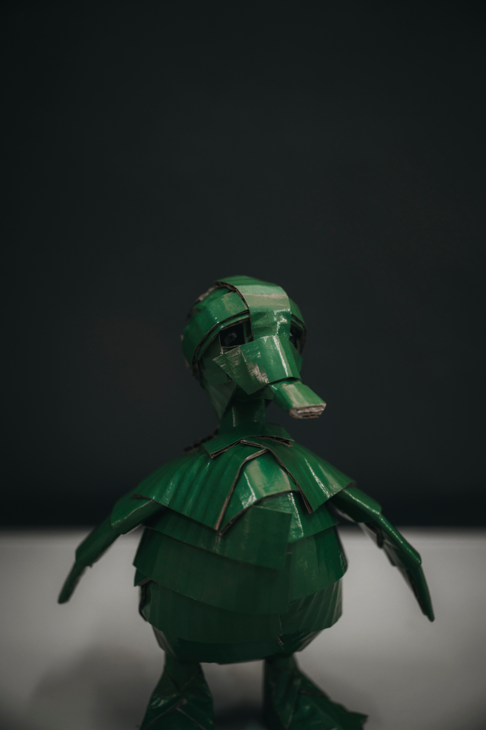 Patito verde inglés de frente, plano medio, fondo negro. Escultura de cartón. Orgaz