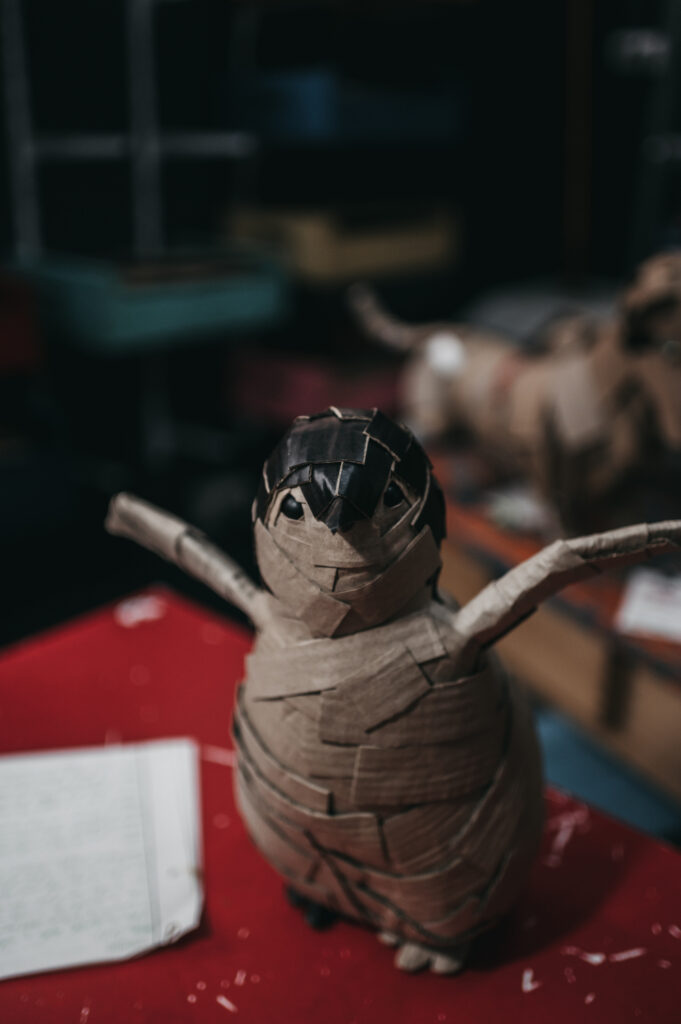 Pichón de pingüino de frente, cuerpo entero. Escultura de cartón.
