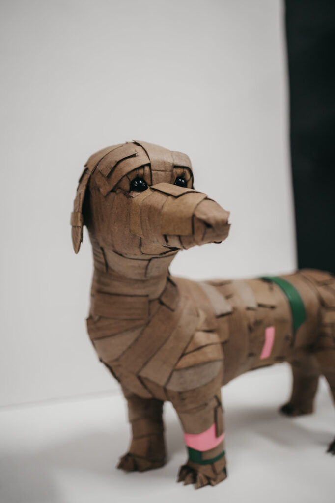 Detalle del teckel rosa y verde de perfil. Escultura de cartón. Orgaz